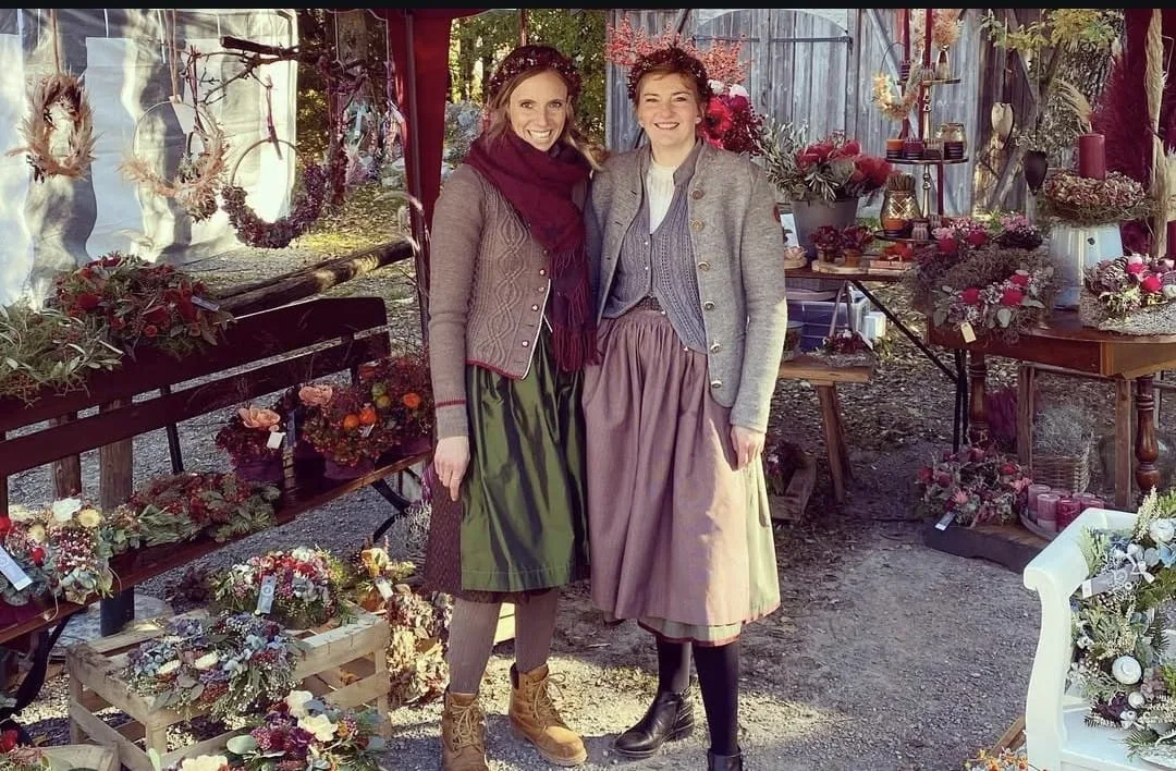 Zwei Frauen in Tracht an einem Marktstand voller Kränze