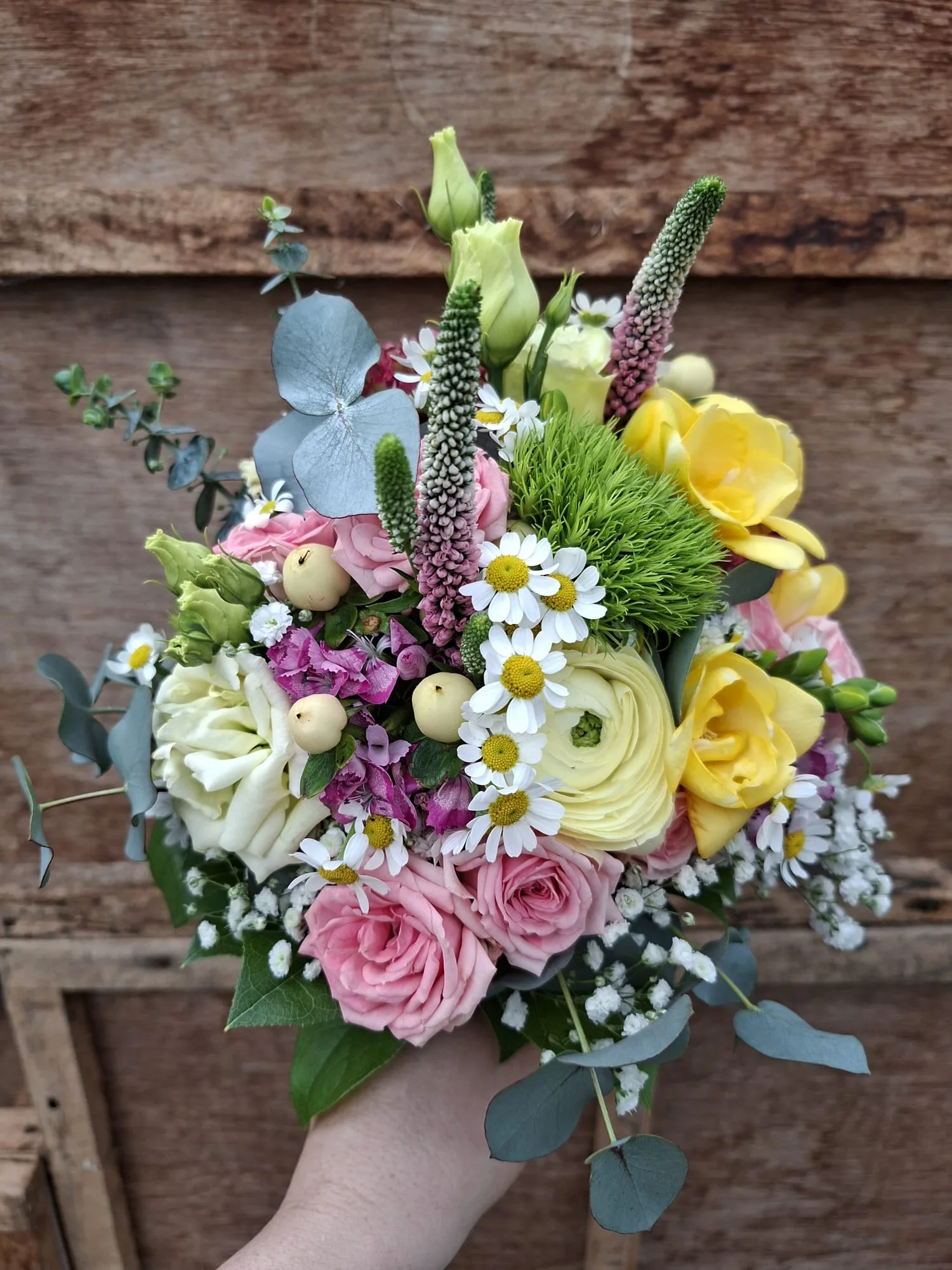 Bunter Strauß mit Rosen, Ranunkeln und Kamille vor einer Holzwand