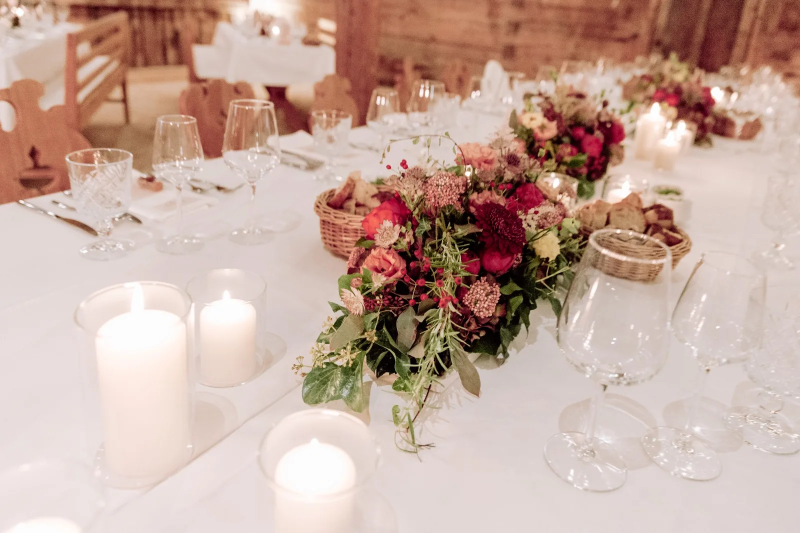 Weiß gedeckte Hochzeitstafel mit niedrigen Gestecken in Rot und Rosa und Kerzen