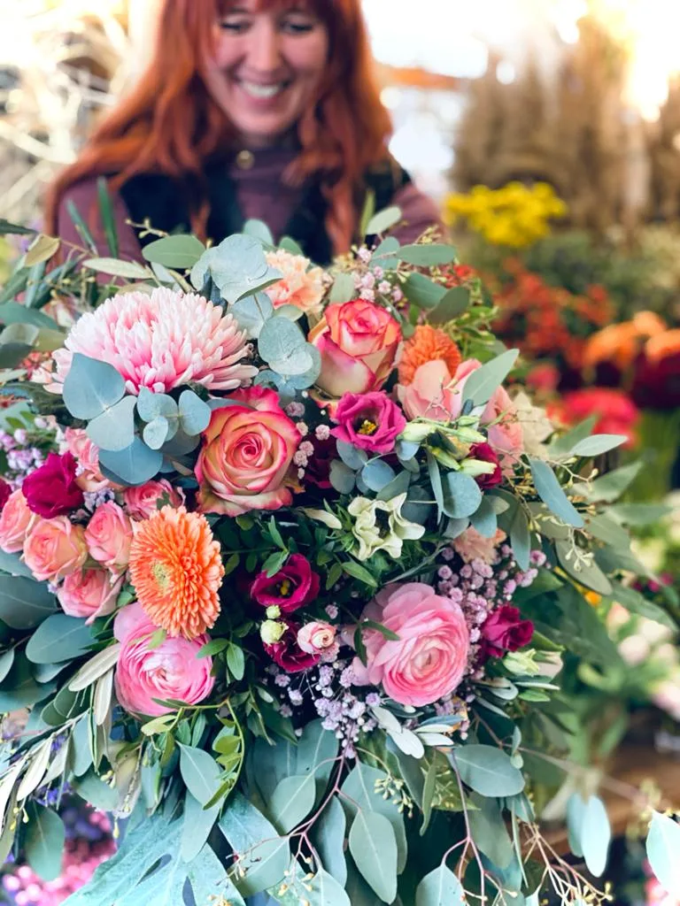 Großer Strauß mit Rosen, Chrysanthemen und Eukalyptus in Rosa und Orange, in den Armen gehalten