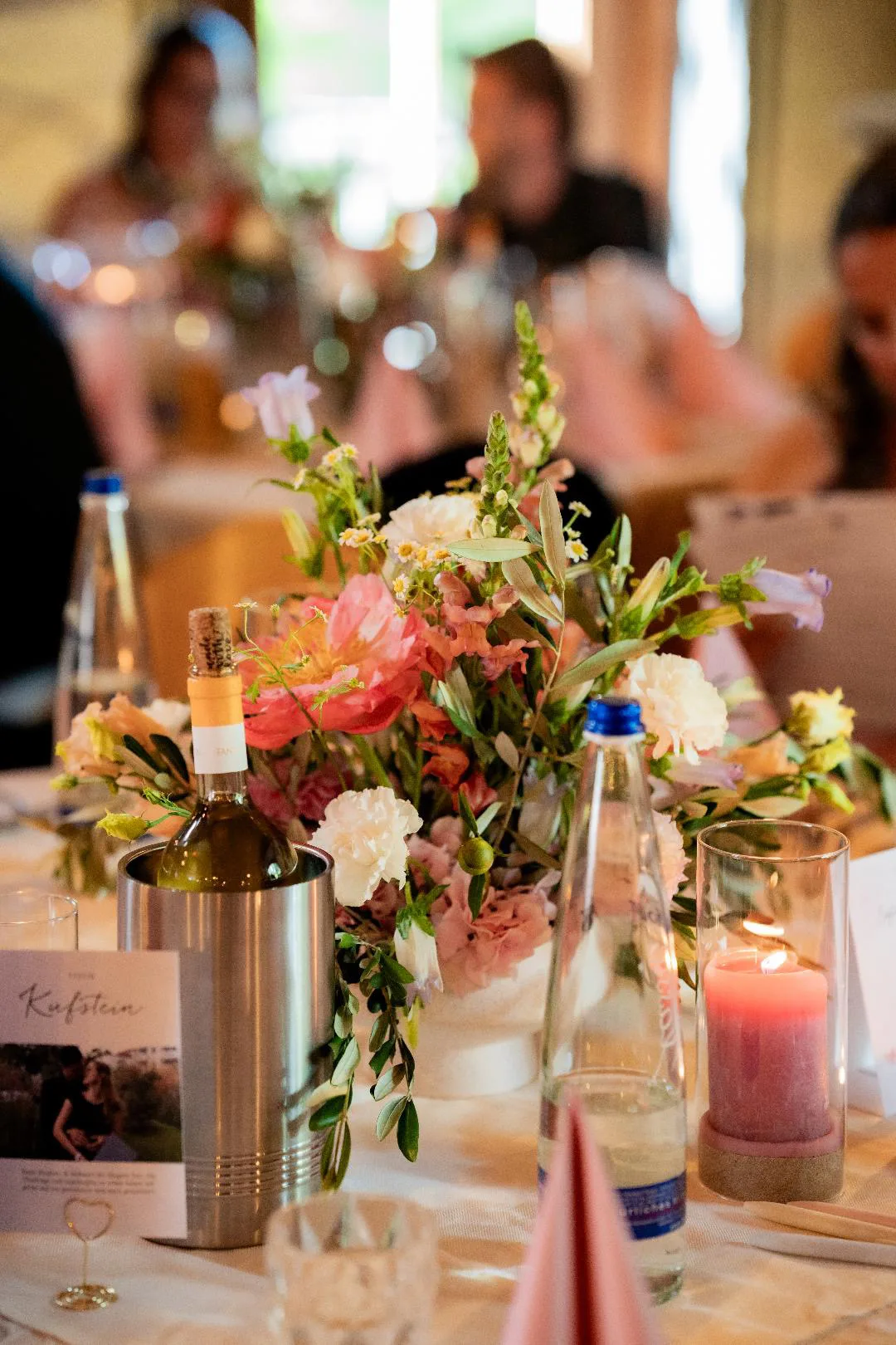 Blumen in einer kleinen Vase neben einer rosa Kerze auf einem gedeckten Festtisch