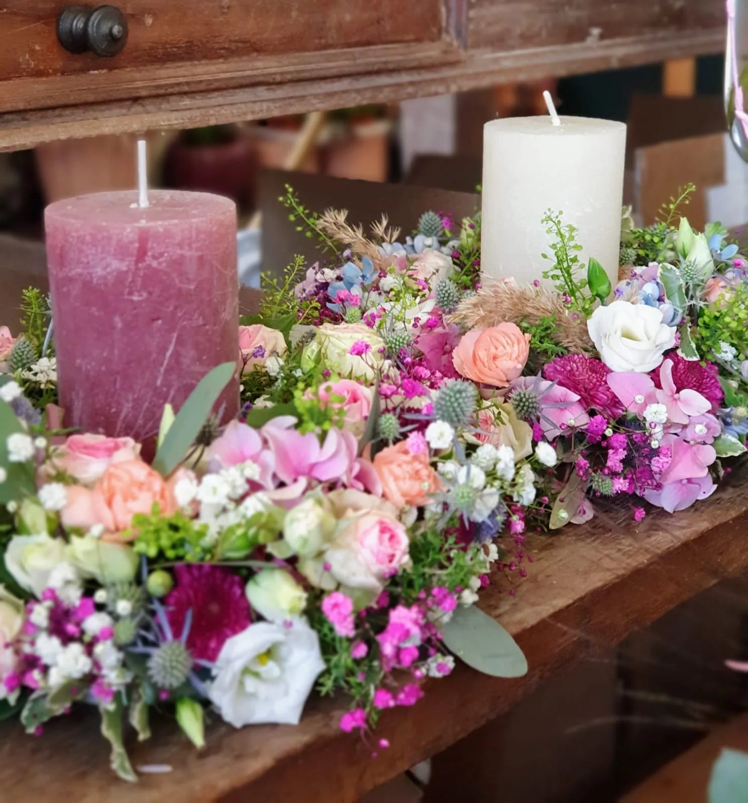 Langes Tischgesteck mit Rosen und Stumpenkerzen in Altrosa und Creme