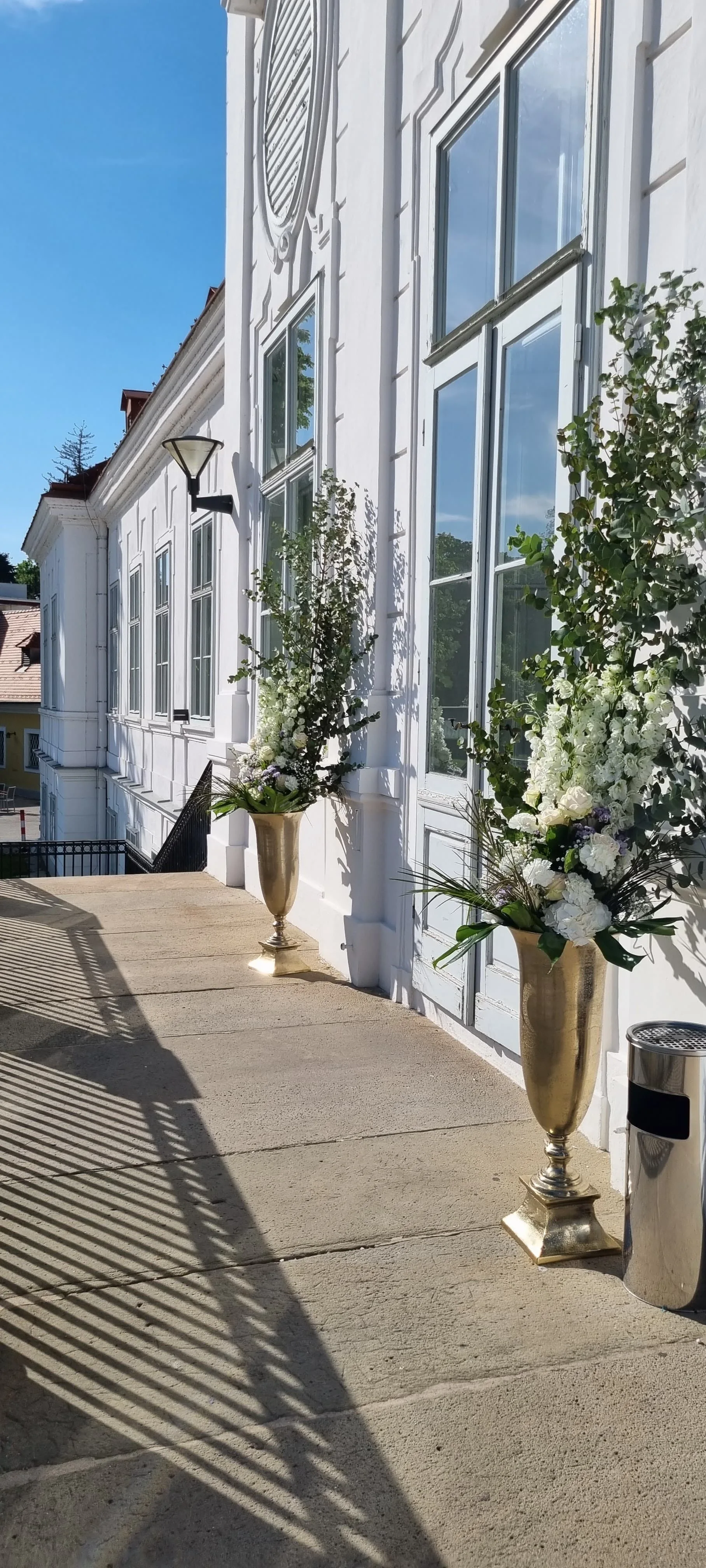 Hohe Arrangements aus weißen Blüten in goldenen Vasen am Eingang eines Gebäudes