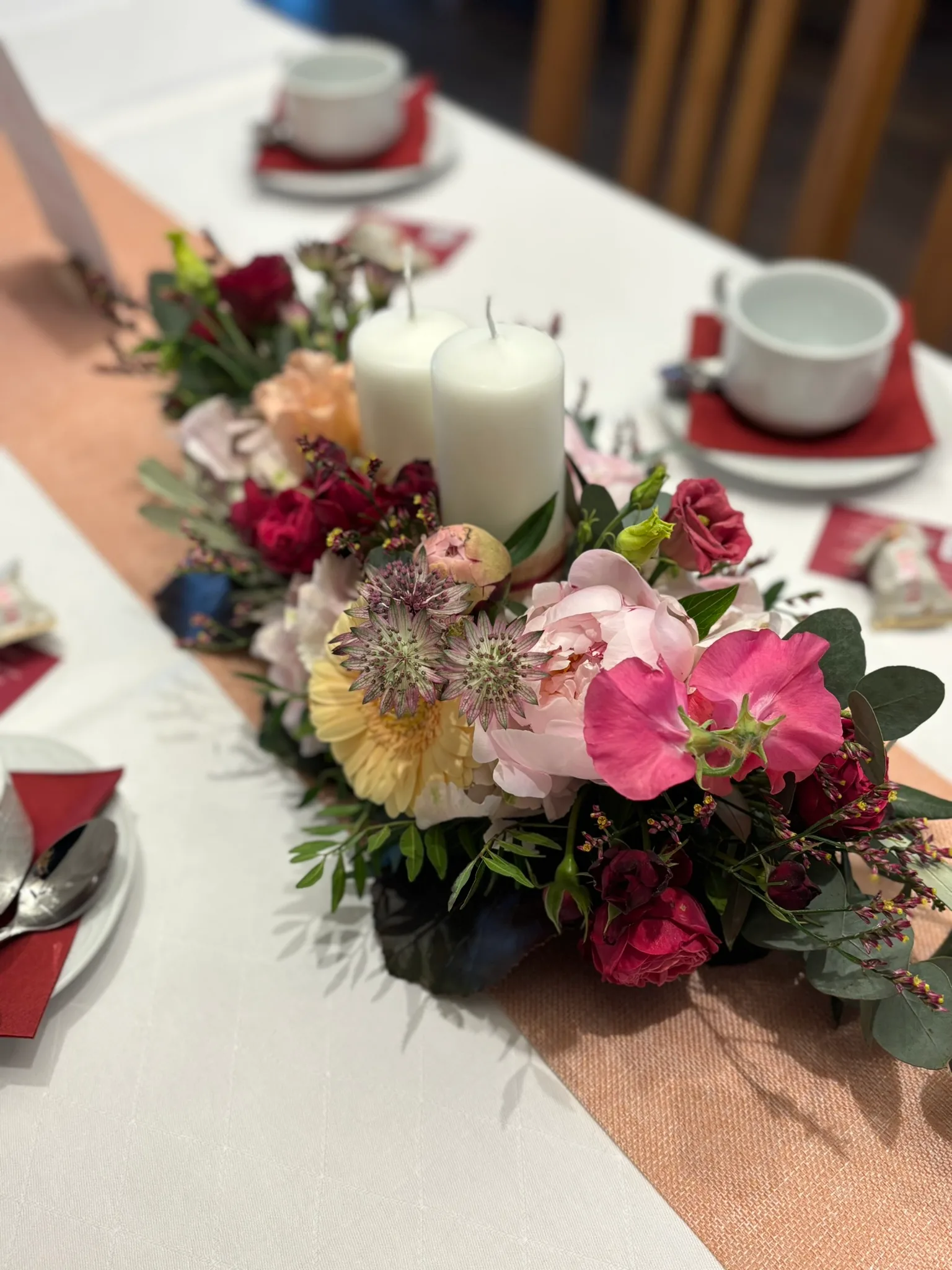 Niedriges Gesteck mit Rosen und weißen Kerzen auf einem gedeckten Tisch
