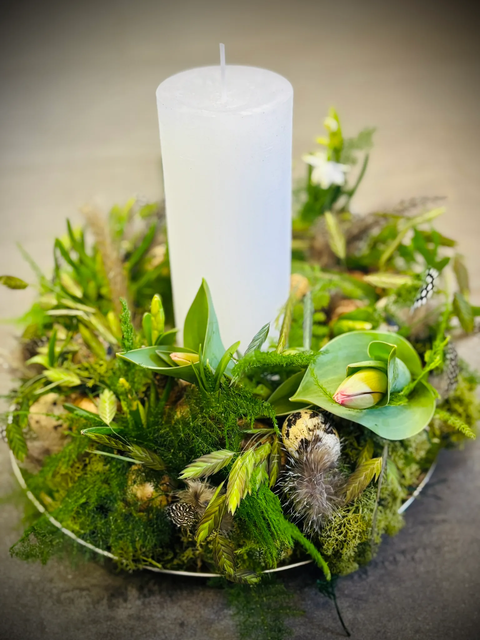 Weiße Stumpenkerze in einem Kranz aus Moos, frischem Grün und einer Tulpe