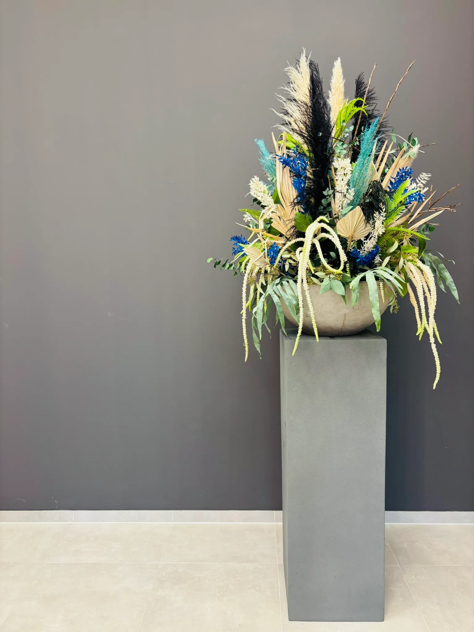 Arrangement aus Trockenblumen und Gräsern in einer Schale auf einer grauen Säule