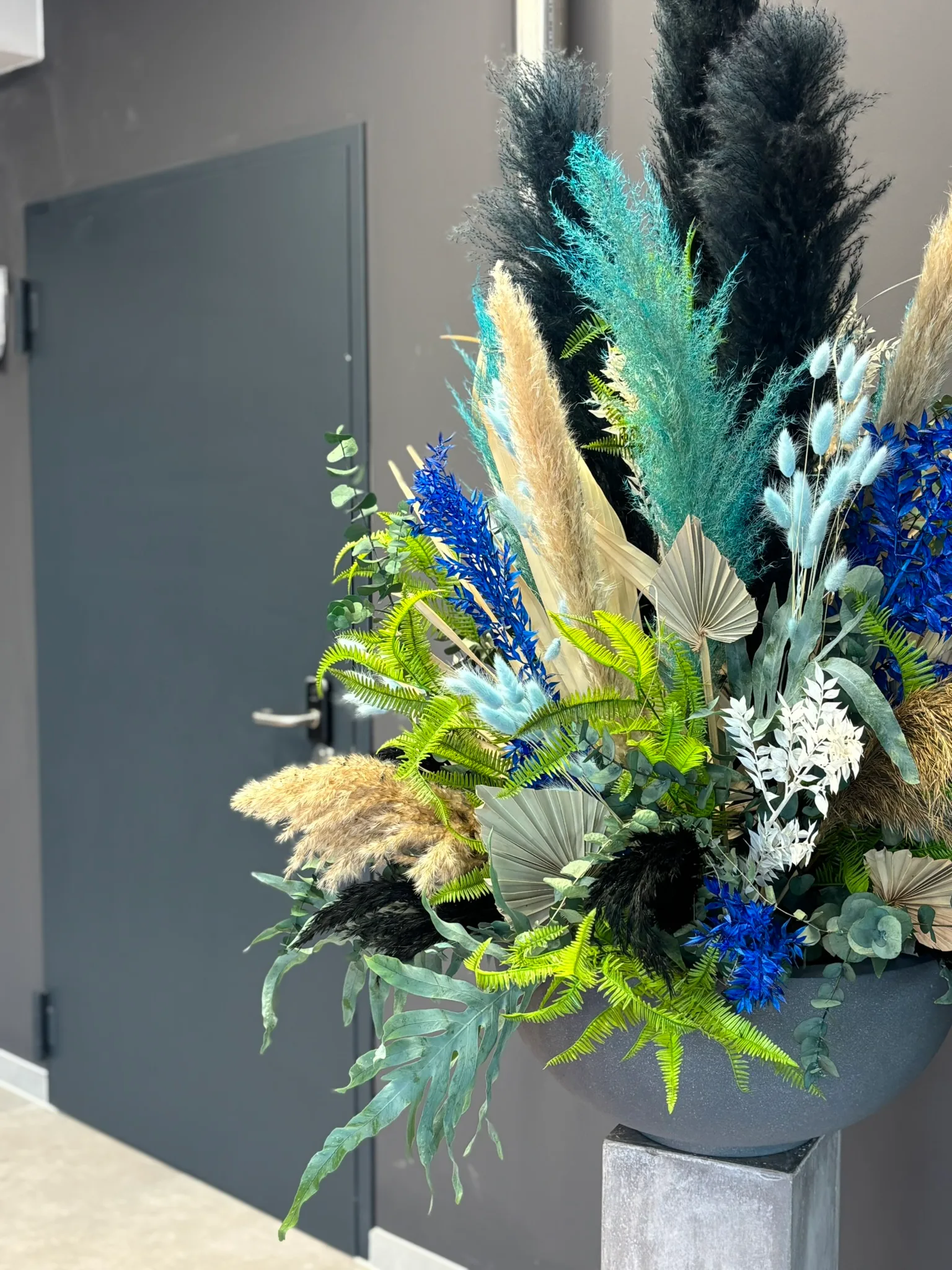 Großes Arrangement aus Trockenblumen und Gräsern in Blau und Grün neben einer Tür