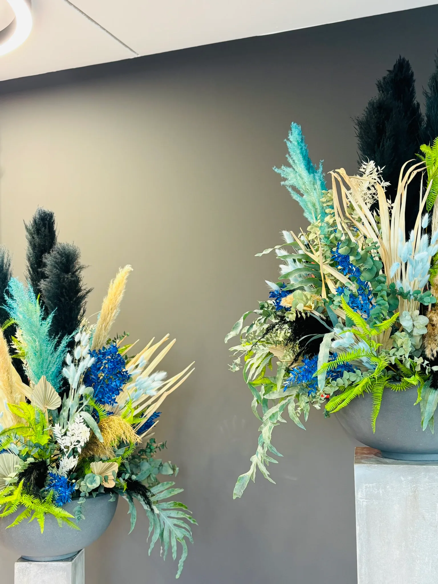 Zwei große Arrangements aus Trockenblumen in Blau, Grün und Creme auf grauen Säulen
