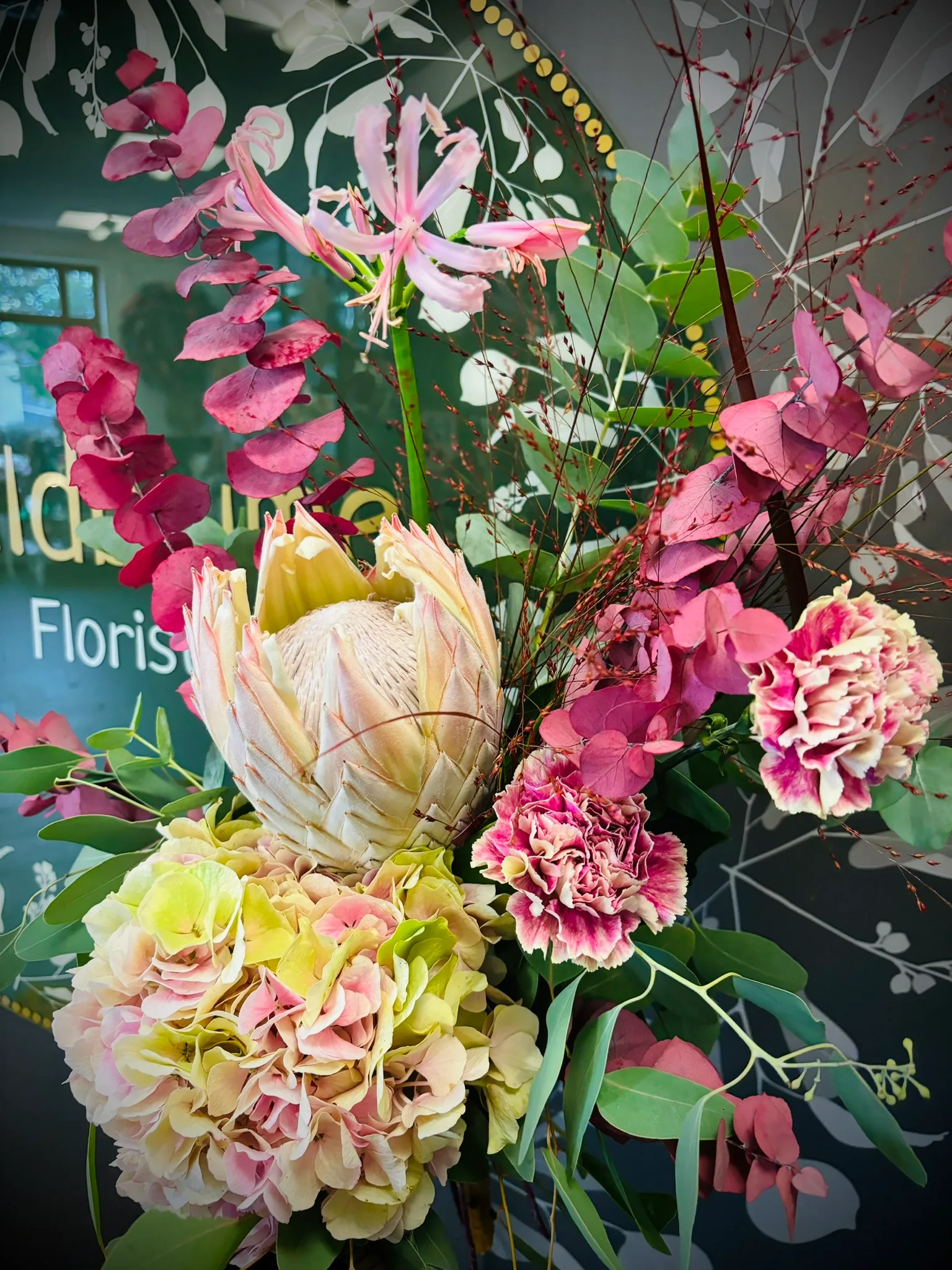 Strauß mit Protea, Nerinen und Hortensien vor dem runden Wildblume-Schild