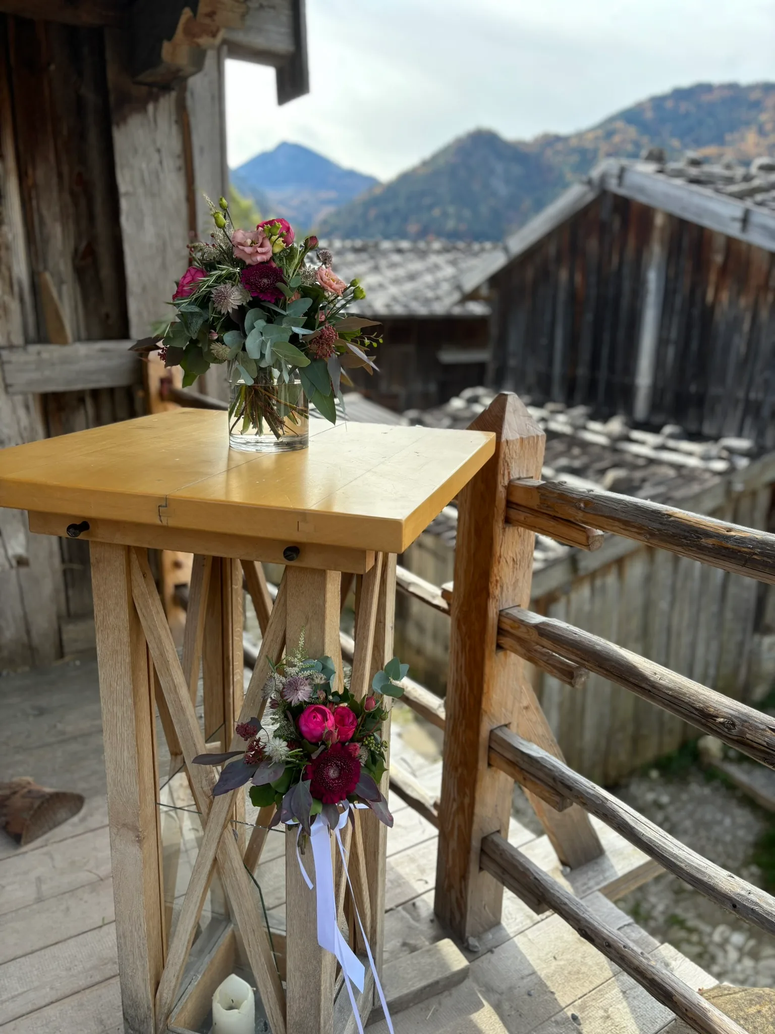 Stehtisch mit einem Blumenstrauß in der Vase auf dem Holzbalkon einer Berghütte