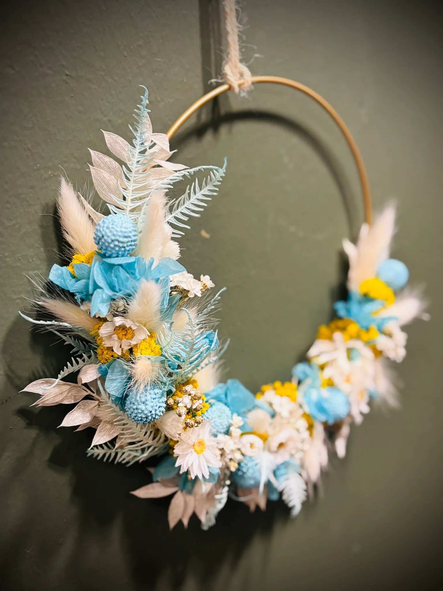 Trockenblumen-Loop in Hellblau und Creme an einer grünen Wand