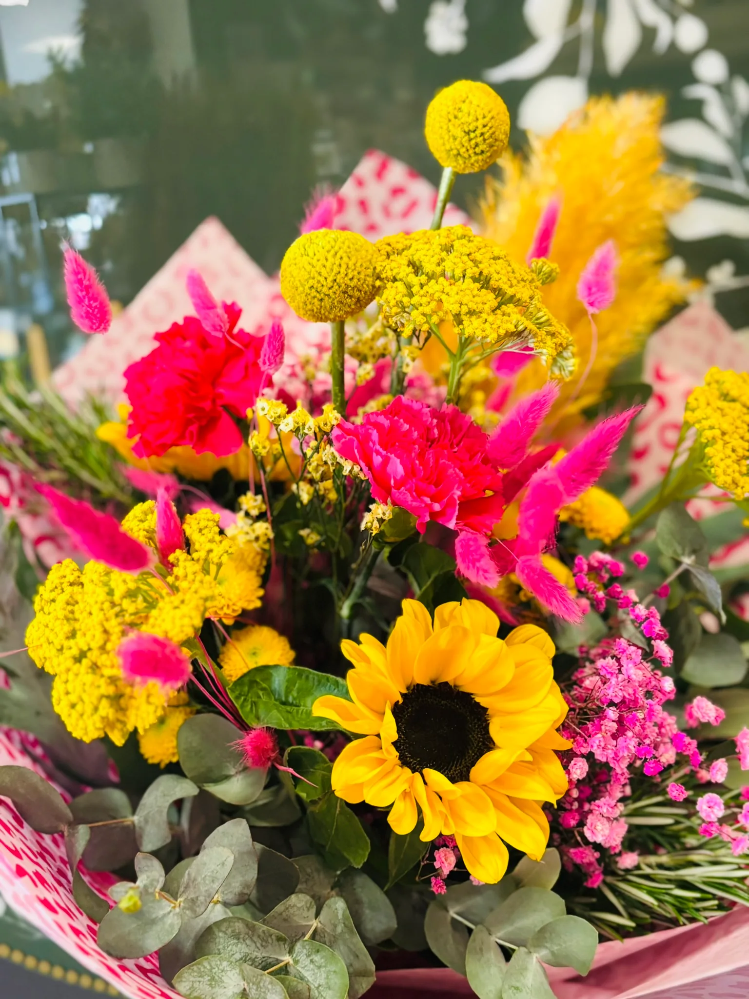 Bunter Strauß mit Sonnenblume, Schafgarbe und Nelken in Gelb und Pink, in Papier verpackt